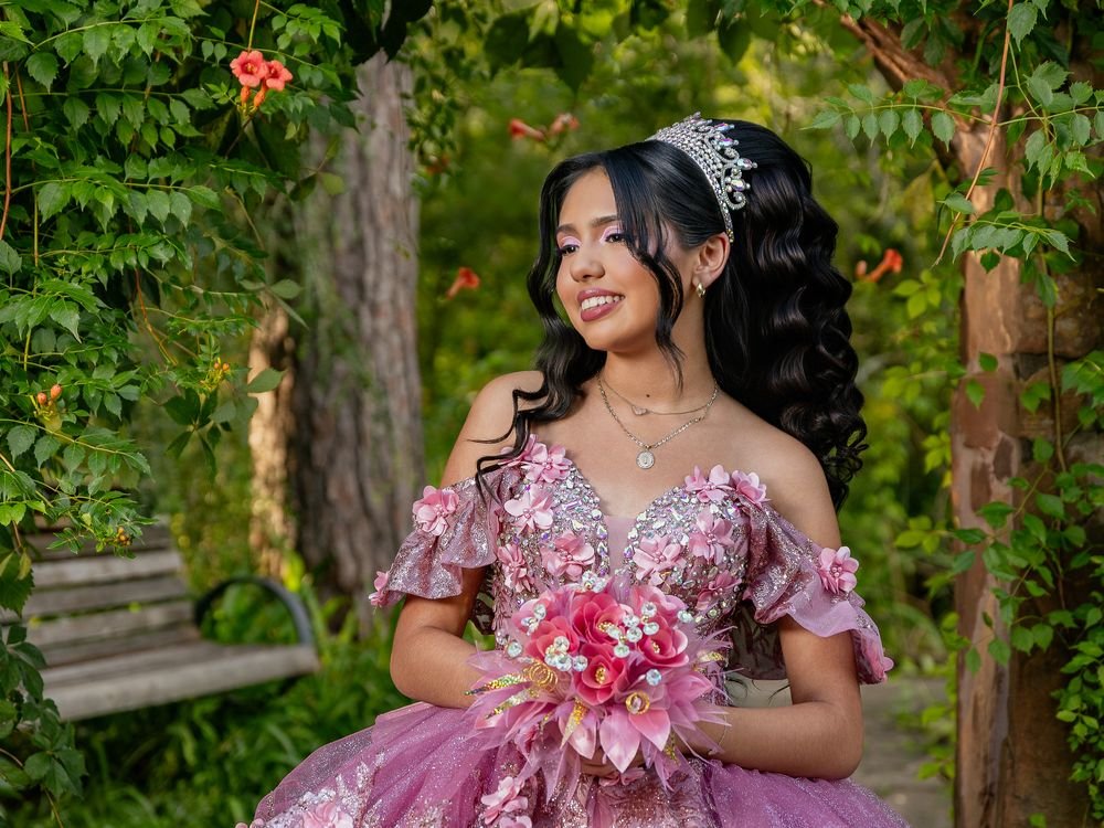 Quinceañera in a pink gown with tiara and bouquet in a garden